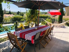 Eine Terrasse im Freien mit Tisch für zwei Personen, umgeben von Stühlen, unter einem großen Sonnenschirm.