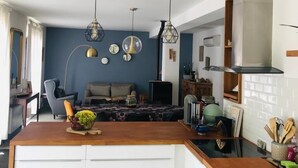 Uma cozinha moderna com armários brancos, bancada de madeira e uma ilha central com uma cesta de frutas. Há luminárias pendentes sobre a ilha e um fogão embutido.