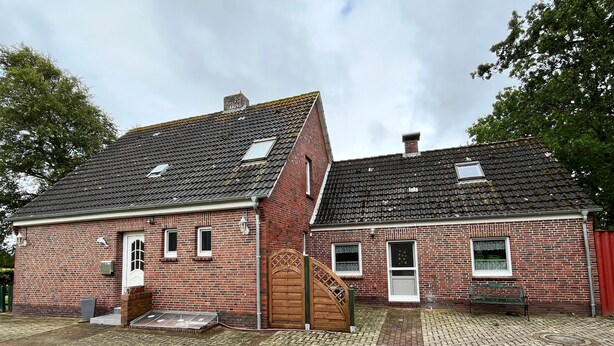 Two brick buildings with tiled roofs, a wooden door, and a paved courtyard. - Vacation home 05 Juliane - W1 (Esens)