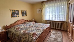 A bedroom with a wooden bed, a nightstand, a radiator, and a window with curtains. - Vacation home 05 Juliane - W1 (Esens)