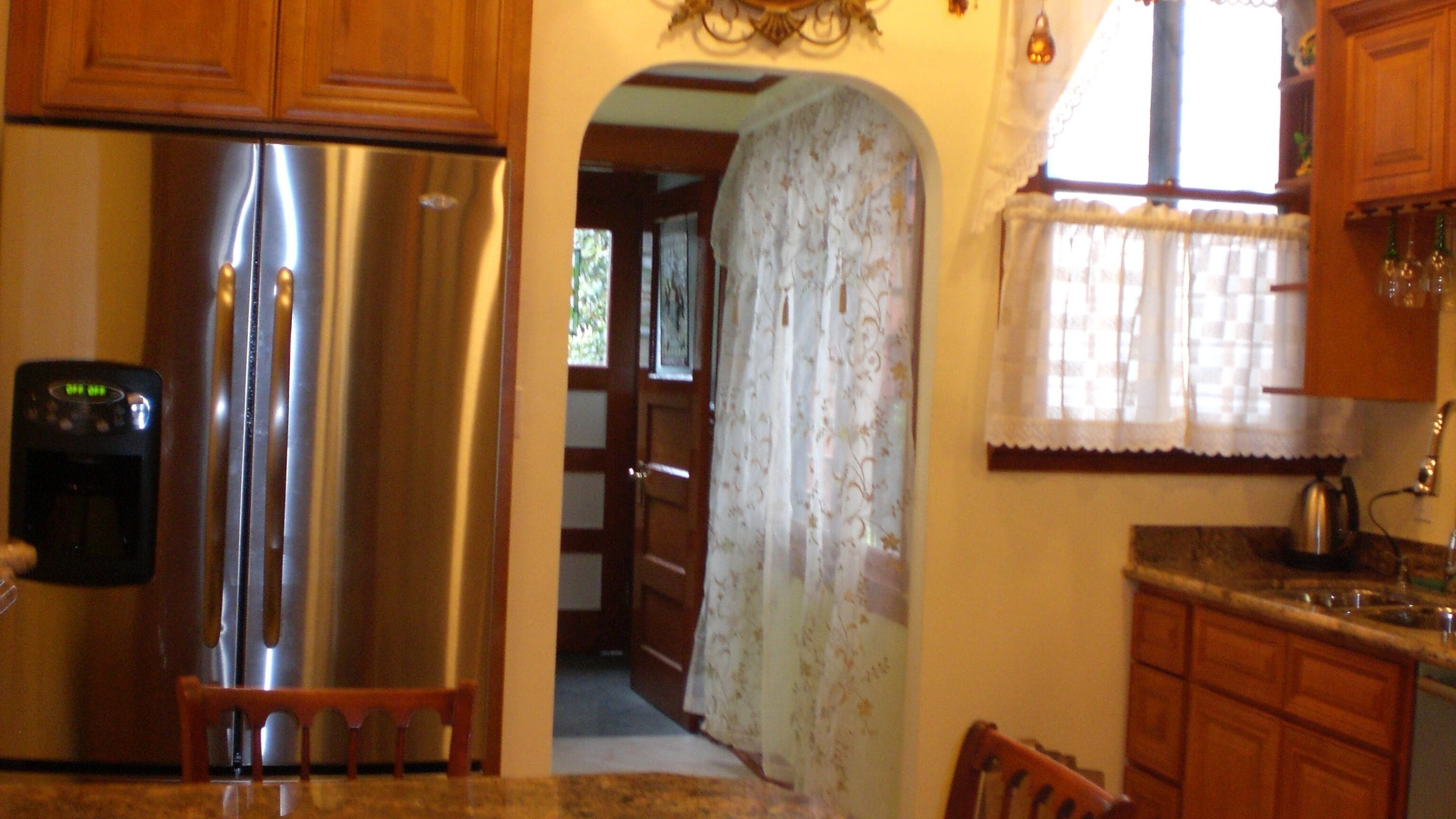 A kitchen with wooden cabinets, a stainless steel refrigerator, a coffee maker, and a window with a floral curtain.