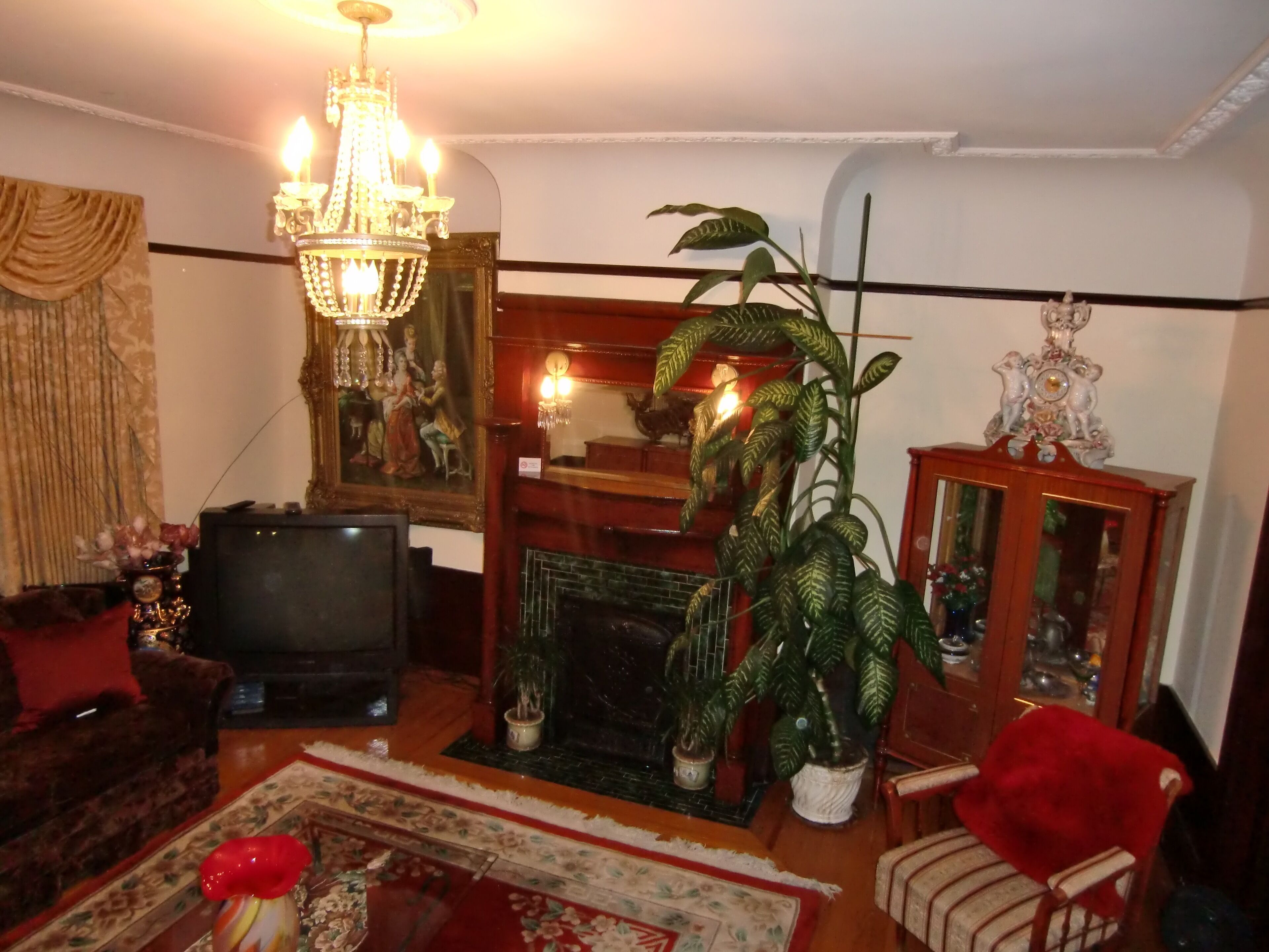 A living room with a chandelier, a television, a fireplace, and a large potted plant.