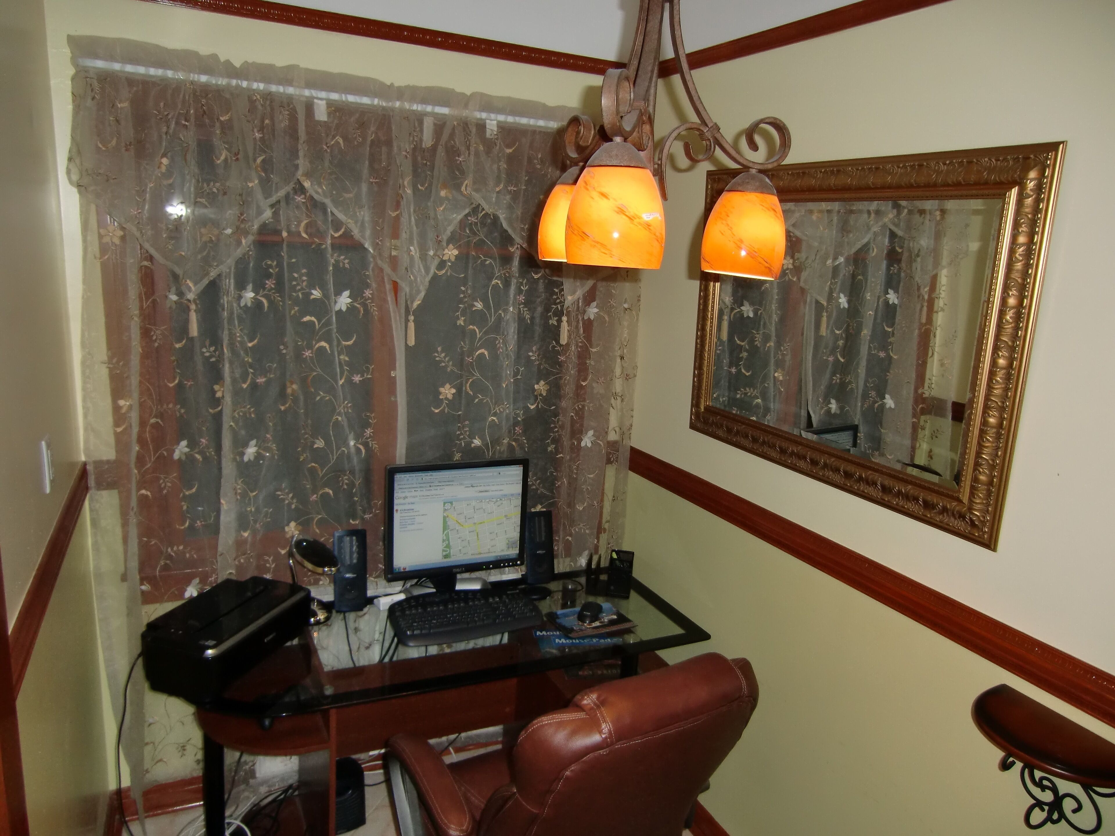 A home office with a computer desk, a chair, a large mirror, and two lamps.