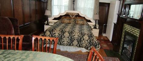A traditional bedroom with a large bed, a fireplace, and a dining table.