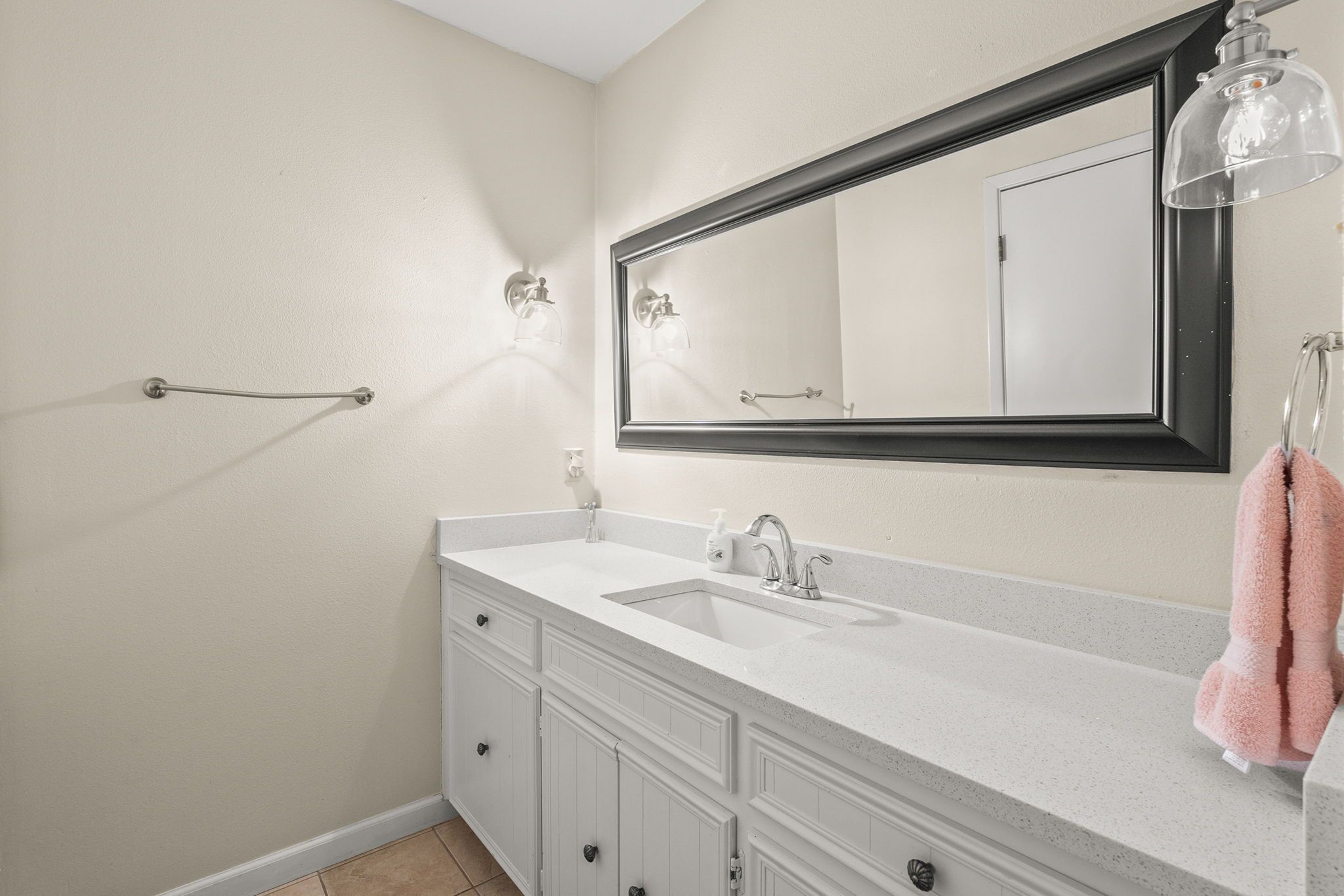 A bathroom with a white vanity, a large mirror, and a towel hanging on the wall.