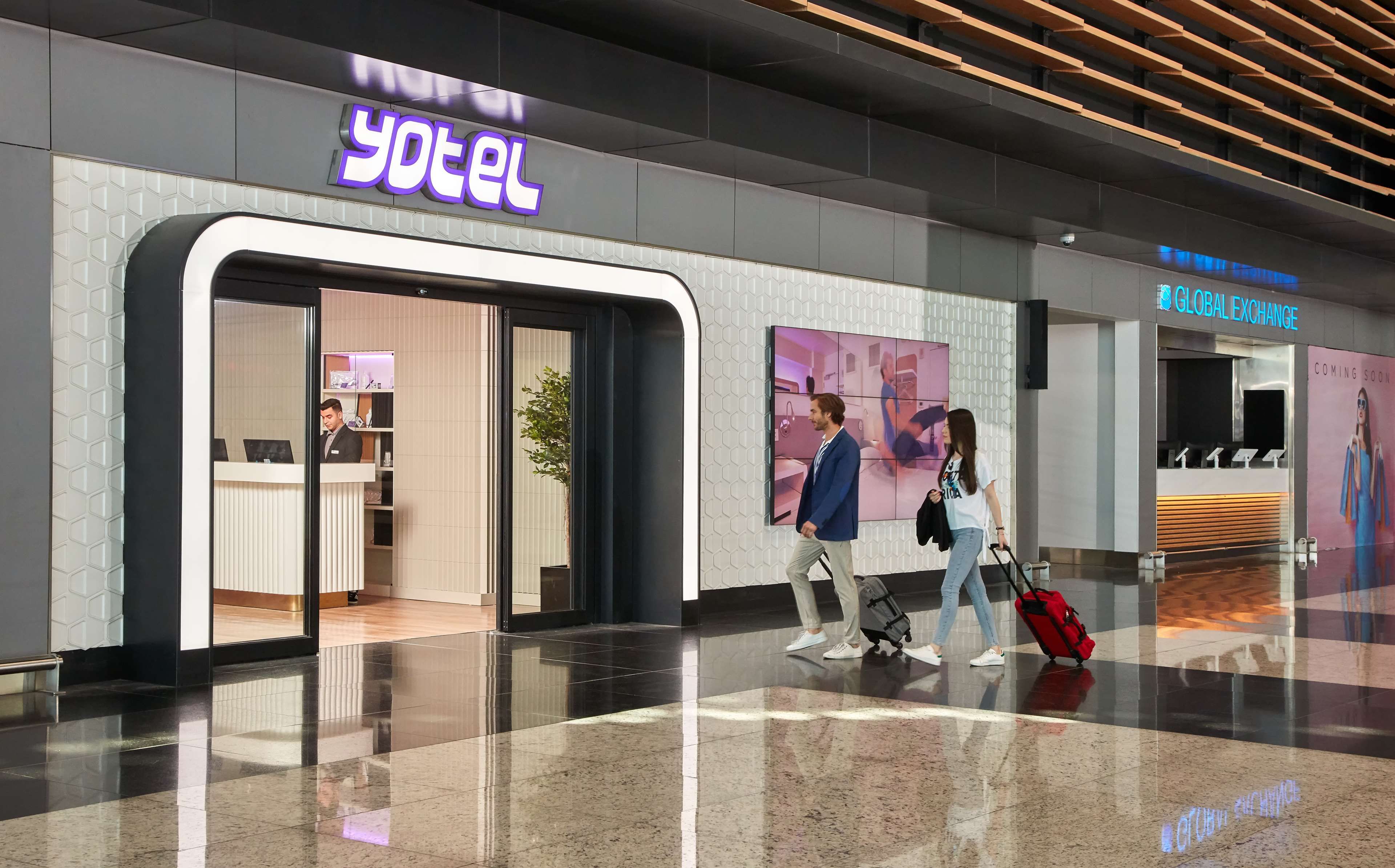 A hotel entrance with a reception desk, a digital sign, and a 'Global Exchange' area.