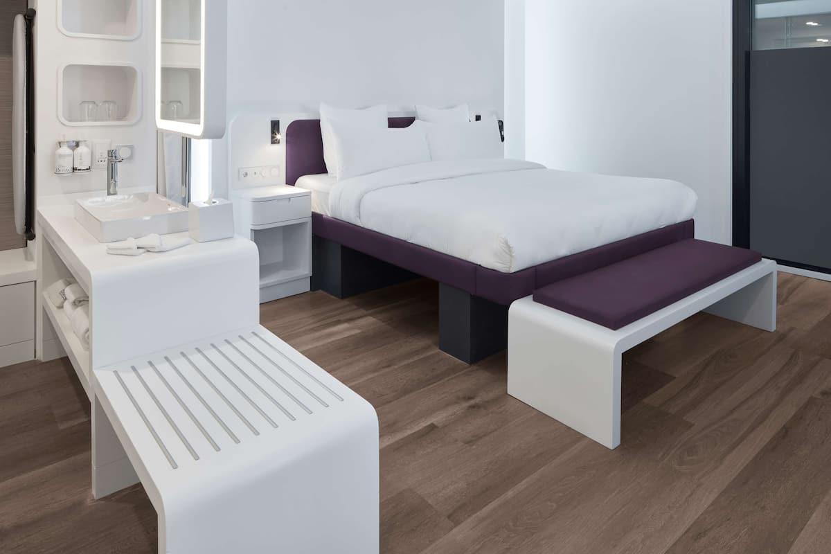 Une chambre moderne comprenant un lit, des tables de chevet, un banc, un miroir et une coiffeuse avec un lavabo.