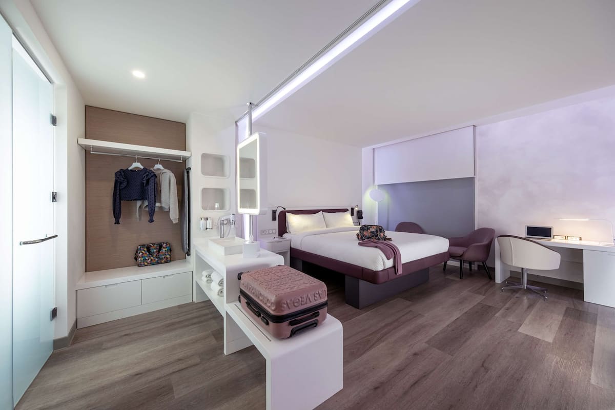 Une chambre d’hôtel moderne équipée d’un lit, d’une table de chevet, d’une armoire et d’un espace bureau.