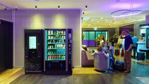 A modern lobby with a vending machine, seating area, and people waiting. - YOTEL Istanbul Airport LANDSIDE, City Entrance  (Arnavutköy)