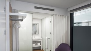 Une salle de bain moderne avec une douche à l’italienne en verre, un lavabo blanc et une chaise violette.