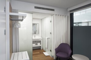 Ein modernes Badezimmer mit einer Duschkabine aus Glas, einem weißen Waschbecken und einem violetten Stuhl.