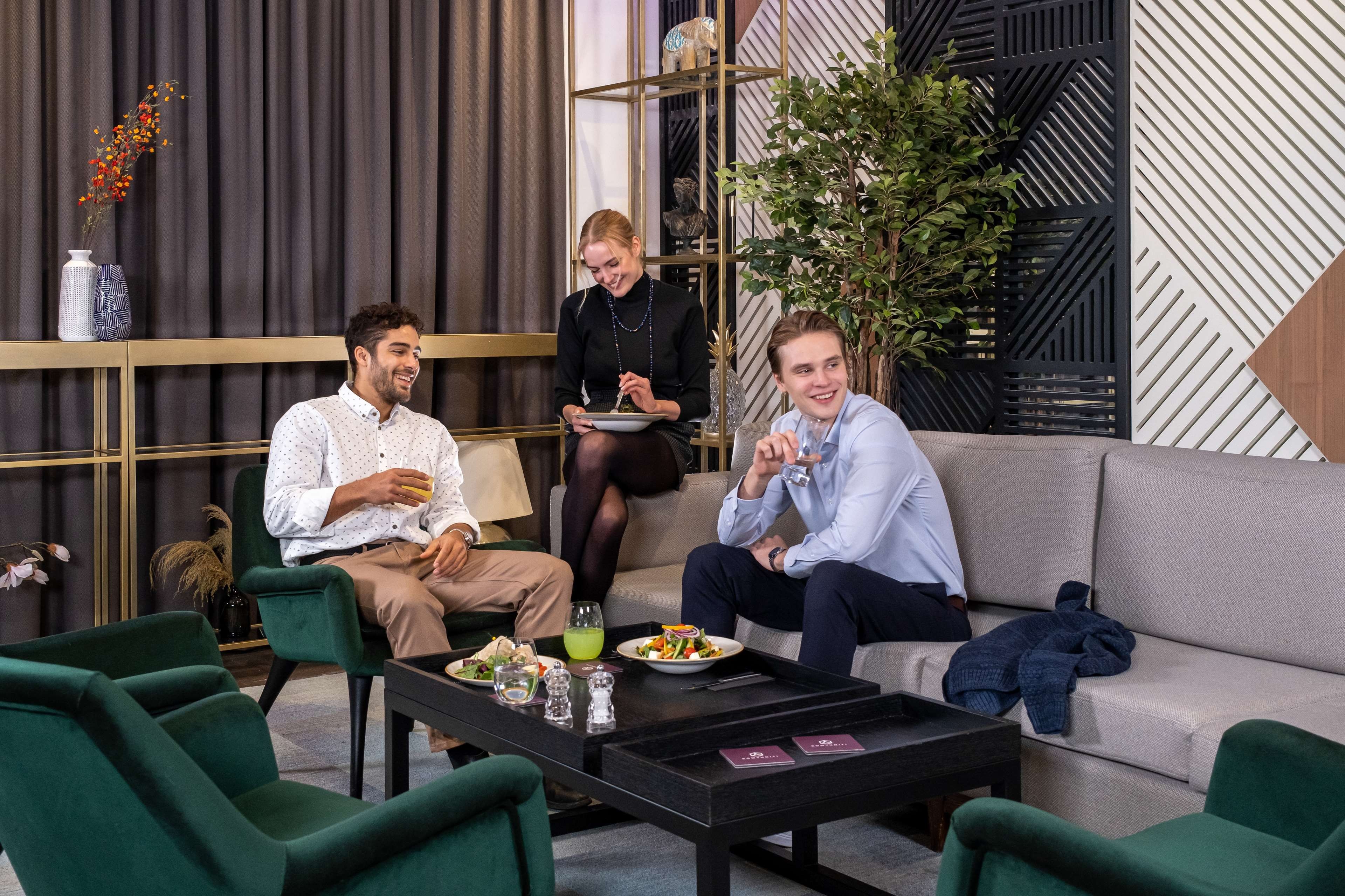A modern interior with a sofa, chairs, a coffee table, and a dining table with food and drinks.