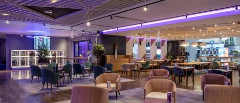A modern hotel lobby with a check-in counter, seating area, and a restaurant.