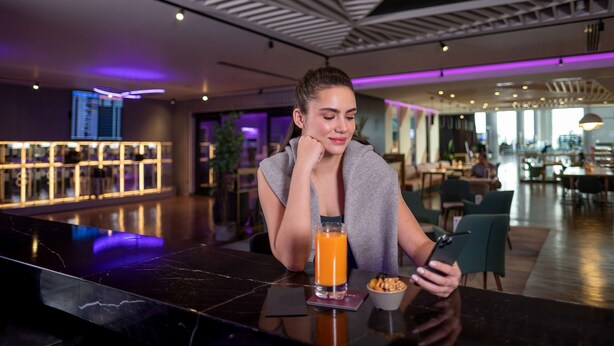 A modern interior with a marble bar, a glass of orange juice, and a person using a smartphone. - YOTEL Istanbul Airport LANDSIDE, City Entrance  (Arnavutköy)