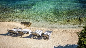 Una playa con agua cristalina, tres tumbonas y una orilla de arena.