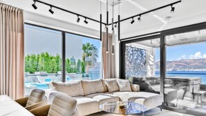 Una sala de estar moderna con un amplio sofá modular, una mesa de centro de vidrio y vistas a una piscina y montañas.