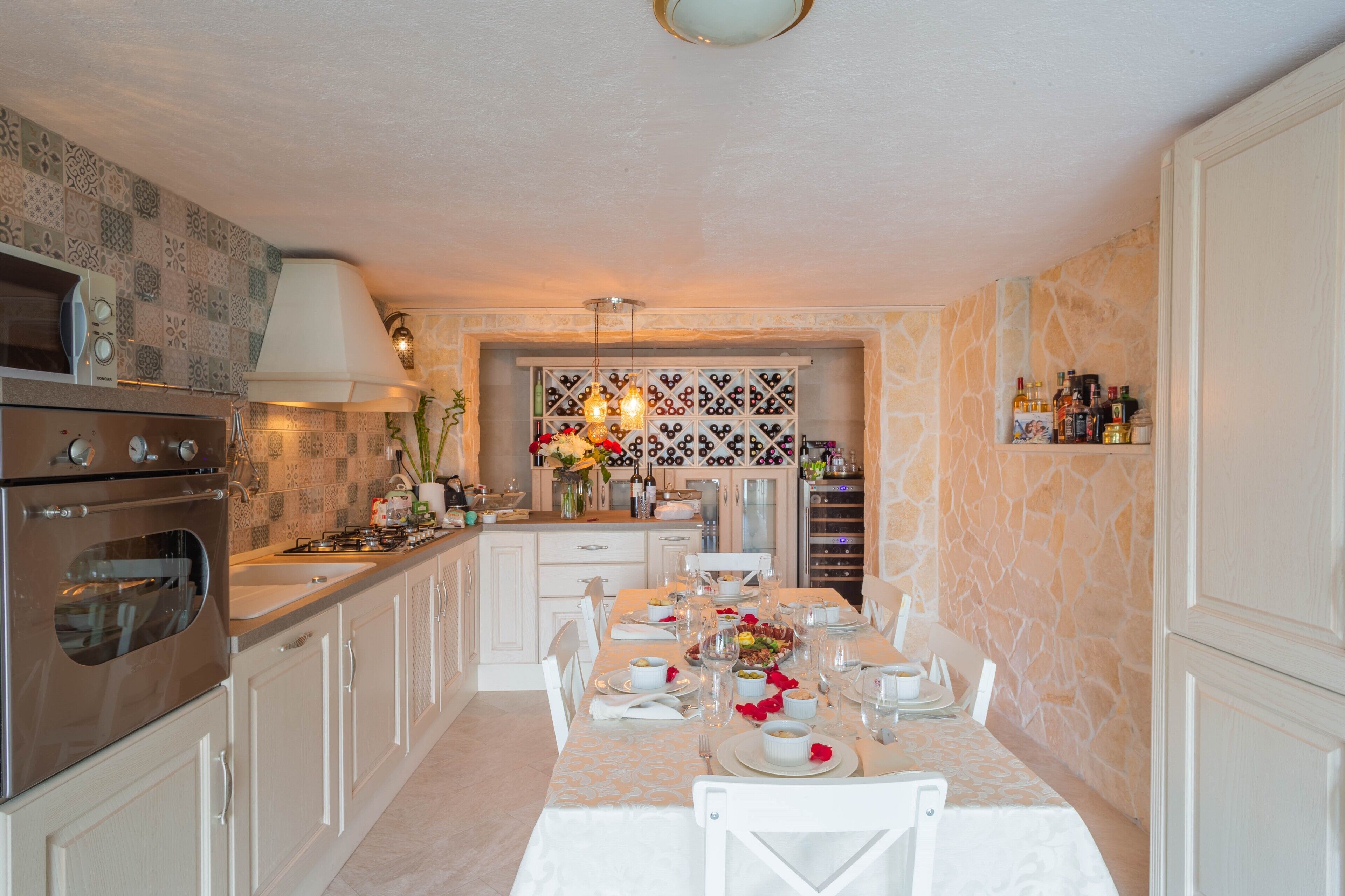 A kitchen with a dining area set for a meal, featuring a stove, oven, and wine rack.