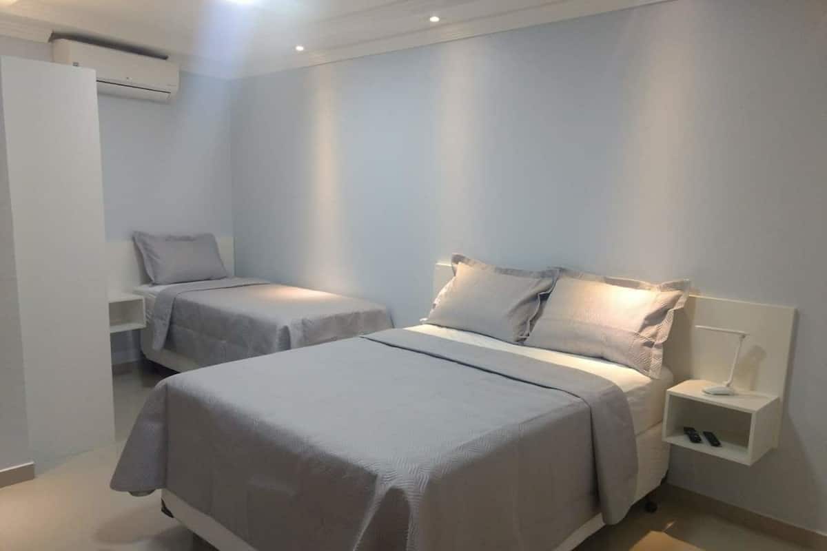 Quarto de hotel com duas camas, uma mesinha de cabeceira com abajur e um guarda-roupa.