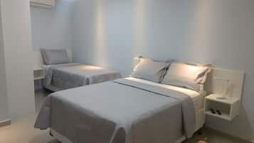 Quarto de hotel com duas camas, uma mesinha de cabeceira com abajur e um guarda-roupa.