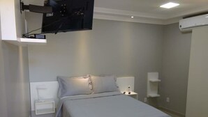 Un dormitorio con cama, mesitas de noche, televisor montado y aire acondicionado.