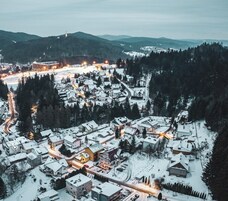 Un pueblo cubierto de nieve con edificios y caminos, rodeado de colinas boscosas.
