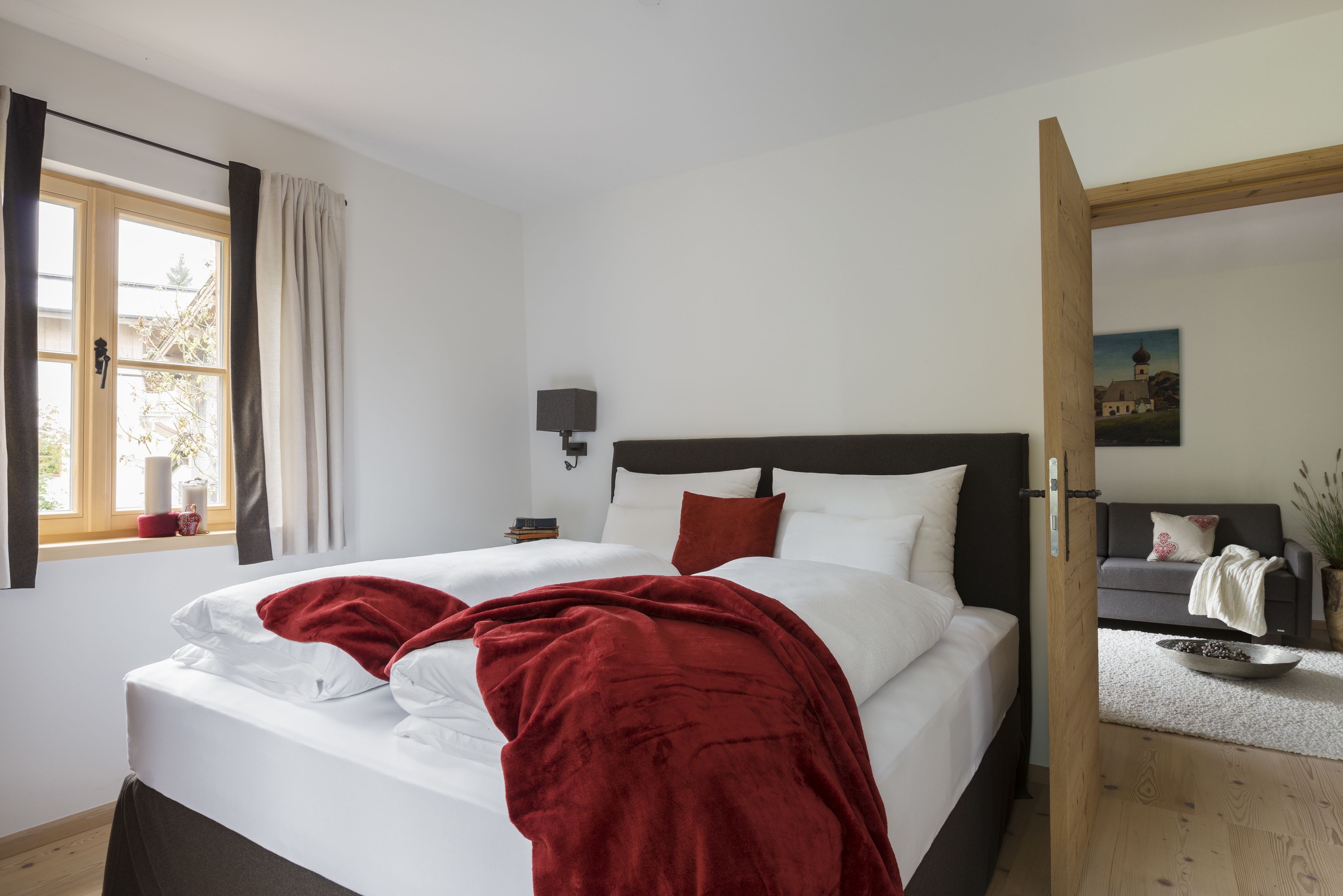 Un dormitorio con cama, mesita de noche, lámpara, ventana con cortinas y un cuadro en la pared.