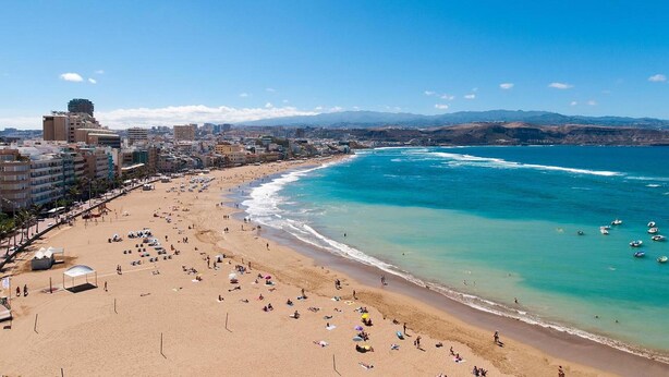 Una playa con vista despejada al océano y un paisaje urbano al fondo.