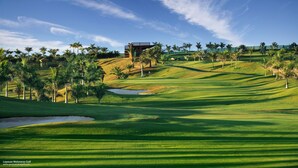 Un campo de golf con un club de campo, palmeras y cielo despejado.