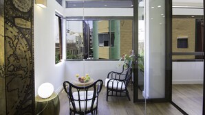 Una habitación de hotel moderna con un ventanal grande, un globo decorativo, una pequeña mesa redonda con fruta y dos sillas de mimbre negro.