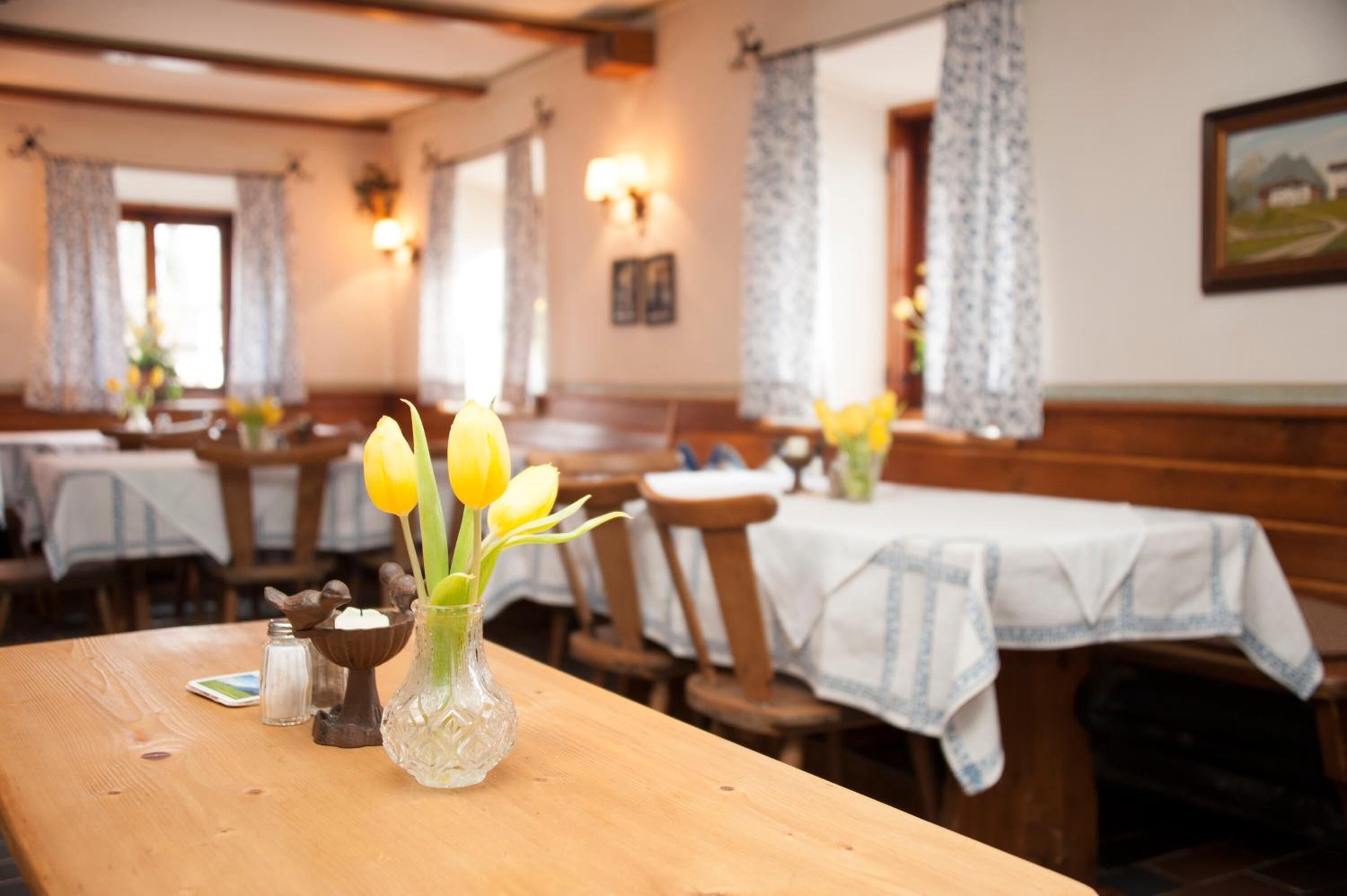 Interno di un ristorante con tavoli di legno, tovaglie bianche e tulipani gialli in vasi.