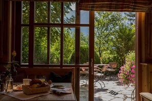 A cozy dining area with a table set for breakfast, a window with a view of greenery, and a patio with outdoor seating.