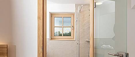 Une salle de bain moderne dotée d’une douche à parois de verre, d’un banc en bois et d’une vue sur l’espace de la douche, visible à travers la porte.