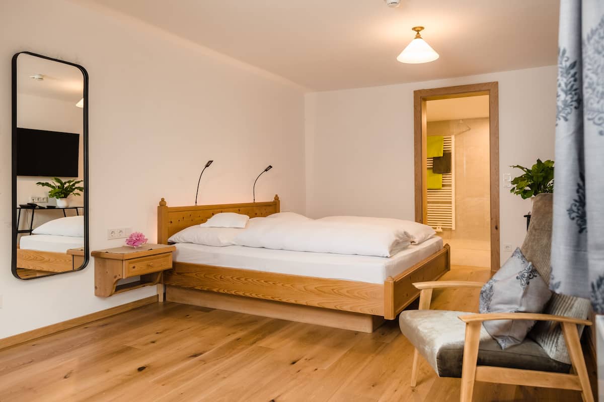 Ein Schlafzimmer mit einem hölzernen Bett, einem Nachttisch, einem Stuhl, einem Spiegel und einer Tür zu einem anderen Raum.