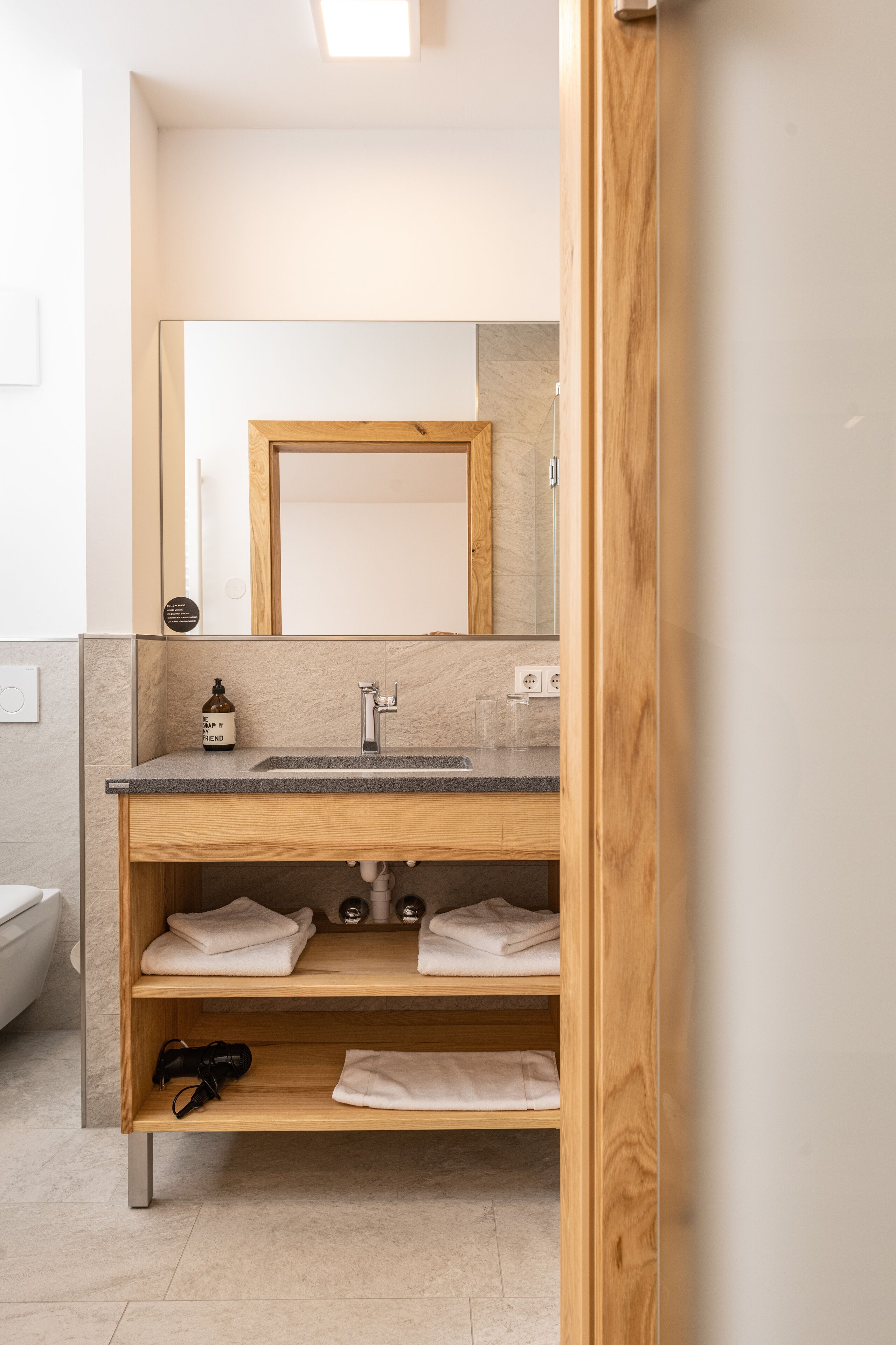 A modern bathroom with a wooden vanity, a mirror, and a sink.