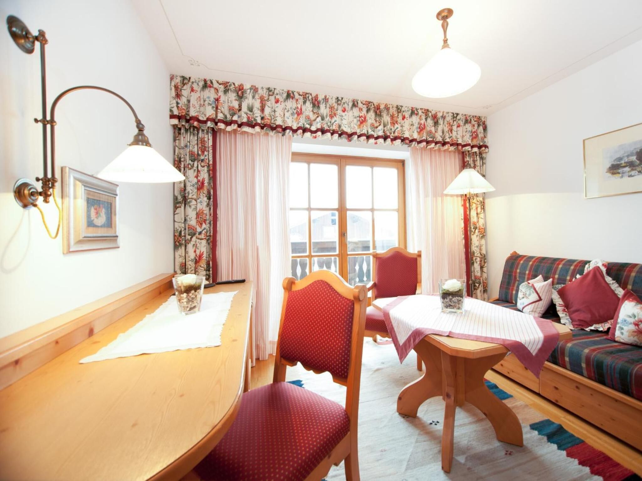 Um quarto acolhedor com uma mesa de madeira, duas cadeiras, um sofá e uma janela com cortinas.