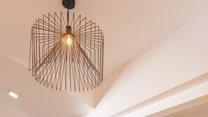 Ein modernes Schlafzimmer mit einem Holzbett, einer einzigartigen geometrischen Deckenleuchte und Blick durch ein großes Fenster.