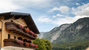 Ein Holzhaus mit Balkonen, die mit Blumen geschmückt sind, vor einer Bergkulisse.