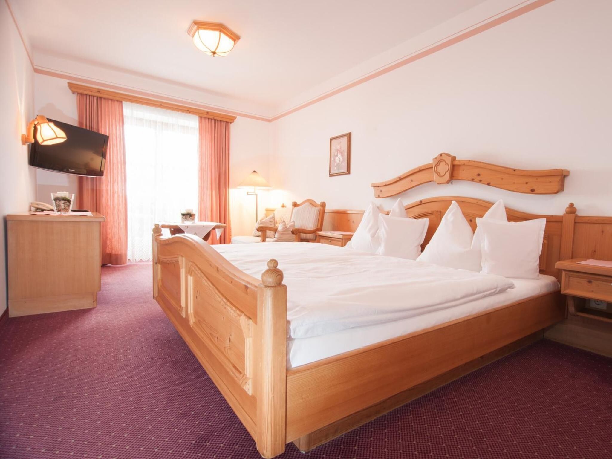 Habitación de hotel con una cama de madera, un escritorio, un televisor y una ventana con cortinas.