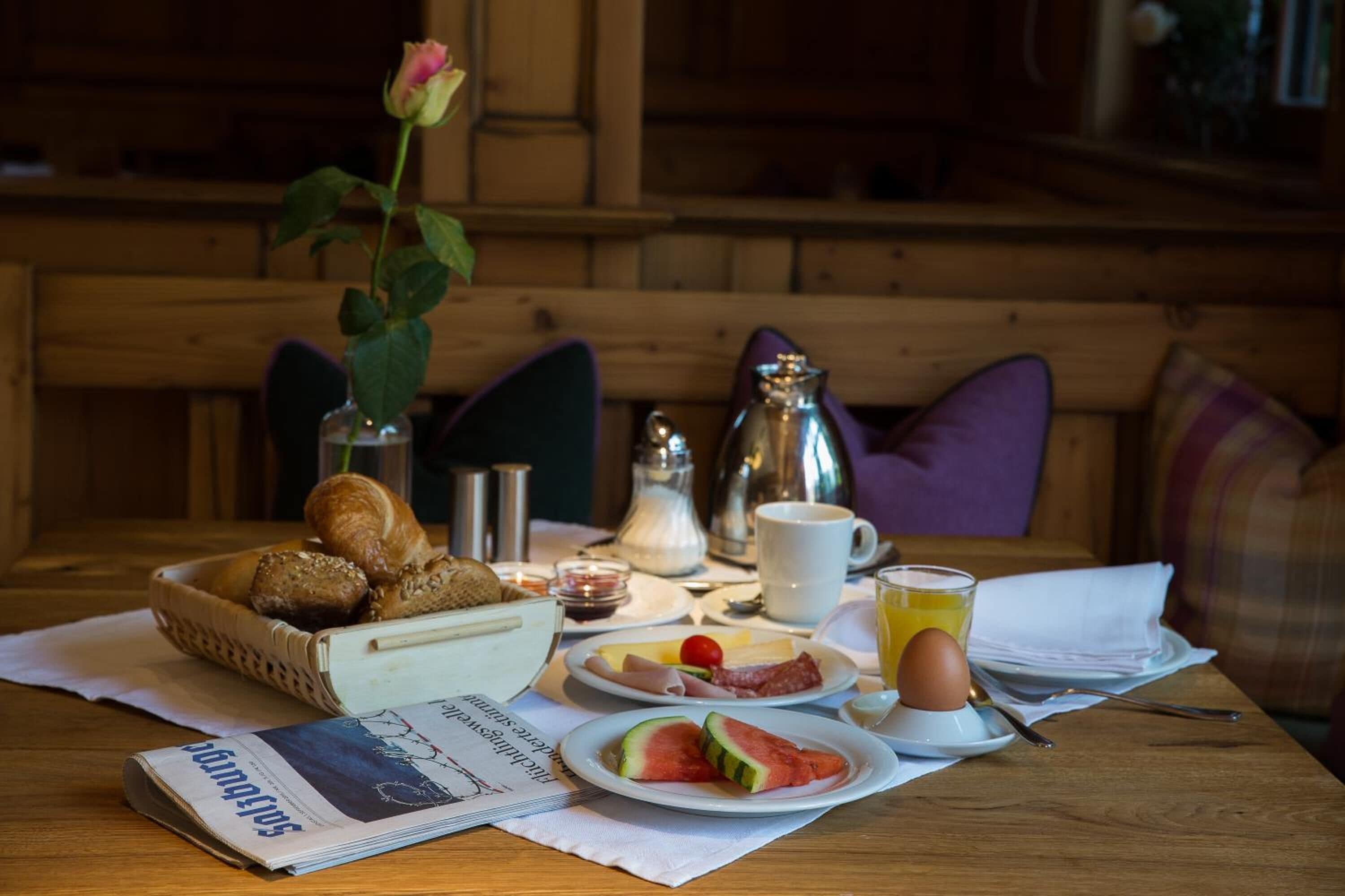 A breakfast table with croissants, a rose, a newspaper, and a variety of breakfast items.