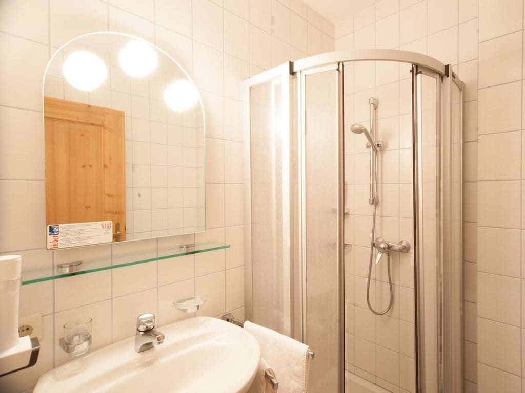 A bathroom with a glass shower enclosure, a sink with a mirror, and a wooden cabinet.