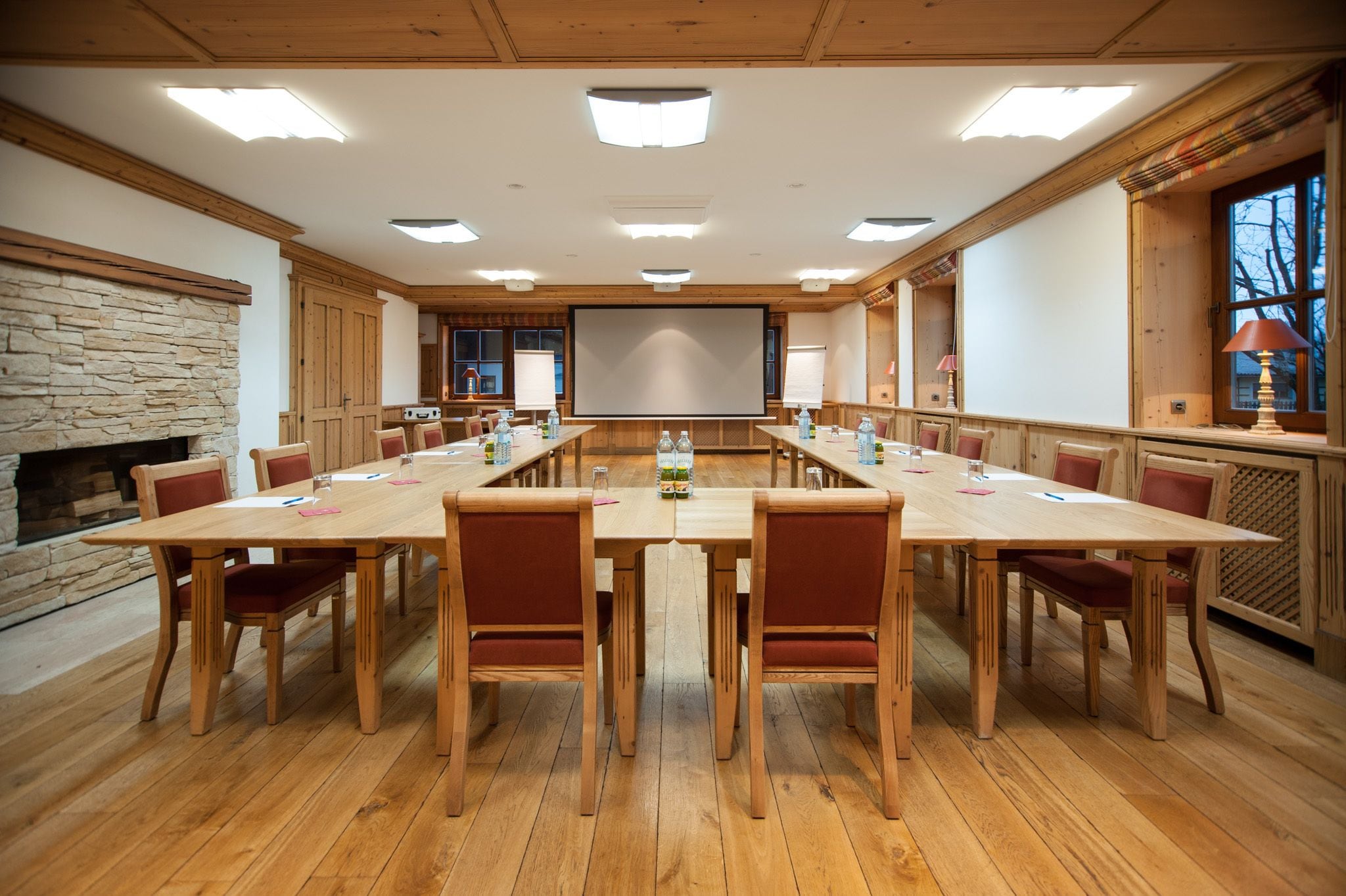 A conference room with a long table, chairs, a projector screen, and a stone fireplace.