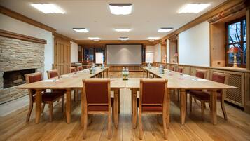 A conference room with a long table, chairs, a projector screen, and a stone fireplace.