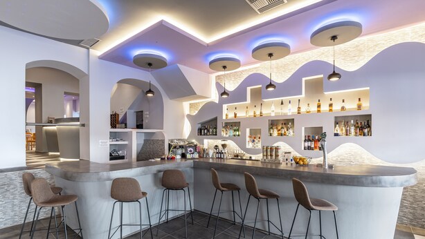 A modern bar area with a curved counter, bar stools, and shelves stocked with bottles. - N E P center Hotel Rodos (Rhodes)
