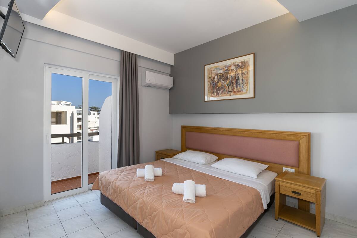 A hotel room with a bed, a nightstand, a painting on the wall, and a sliding door to the balcony.