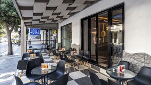 An outdoor seating area with tables and chairs, a hotel sign, and a glass door entrance. - N E P center Hotel Rodos (Rhodes)