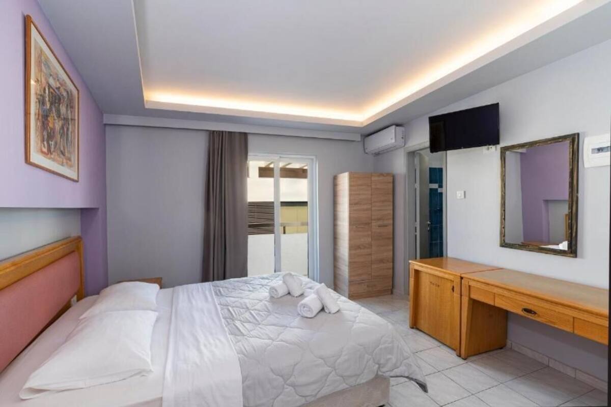 A hotel room with a bed, a wooden desk, a flat-screen TV, and a large mirror.