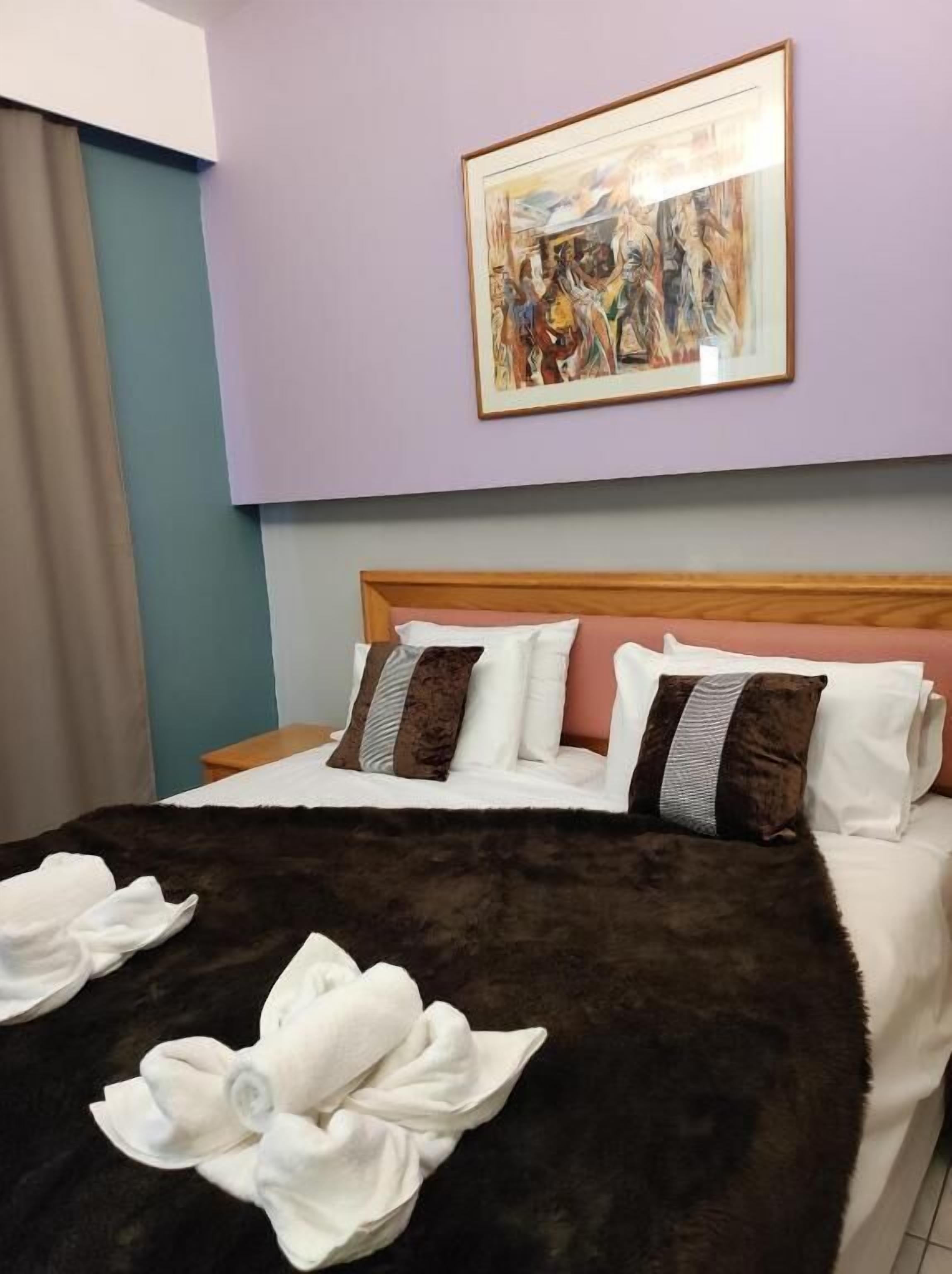 A hotel room with a bed, pillows, a framed artwork on the wall, and a fur throw on the bed.