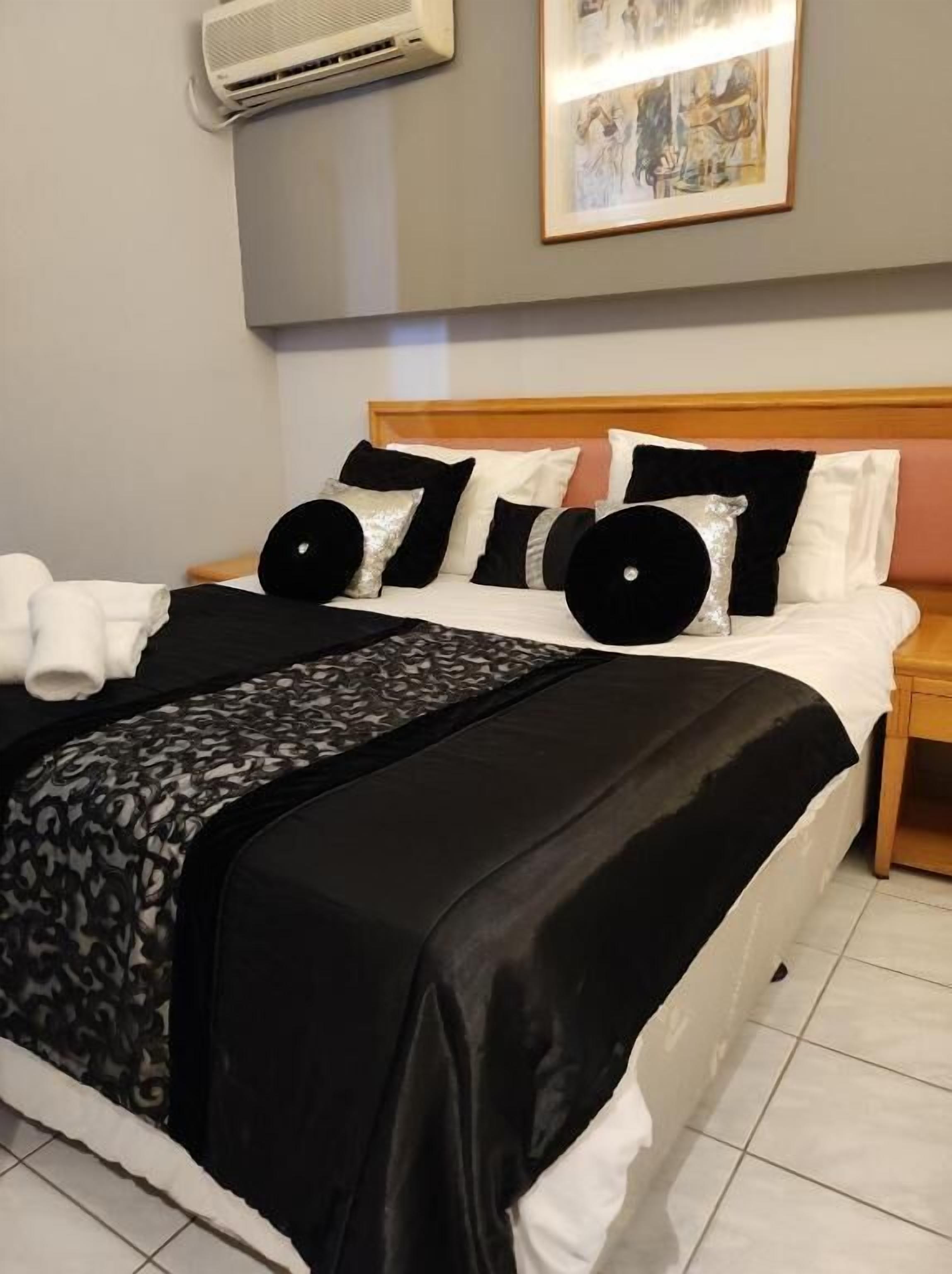 Una cama bien tendida con una colcha blanco y negro, un cabecero y un cuadro enmarcado encima.