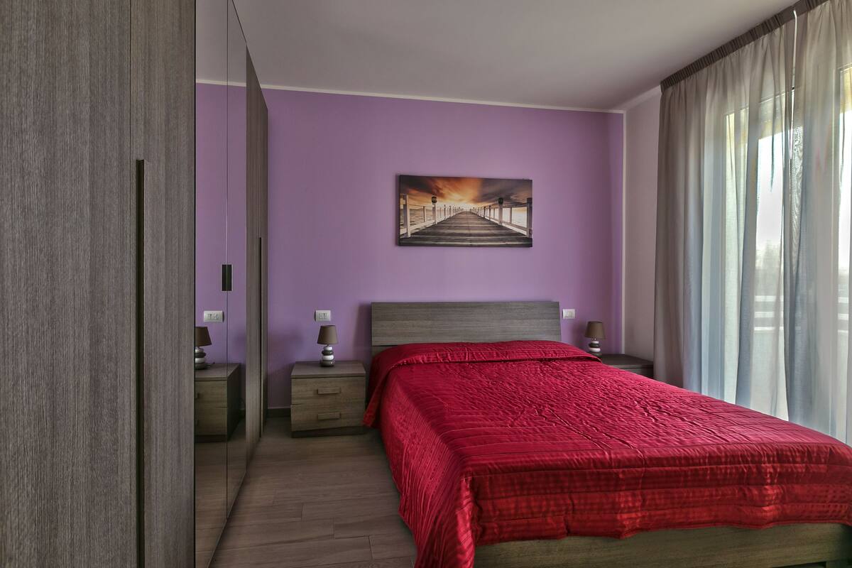 A bedroom with a bed, a nightstand, a lamp, and a painting on the wall.