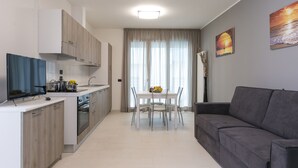 A modern kitchen with white cabinets, a dining table with chairs, and a grey sofa. - Residenza Riva Azzurra (Rimini)